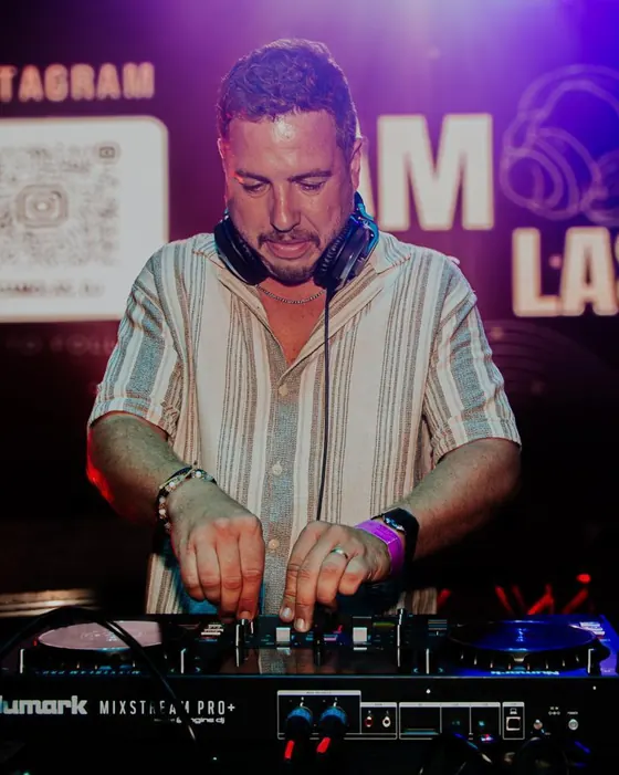 Retrato do Camolas DJ na cabine, com auscultadores ao pescoço, em frente ao logótipo Camolas